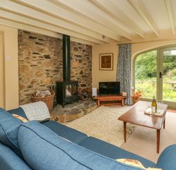 A living room with blue sofas a wood stove and a wooden coffee table in front of glass doors at Taibach in Dinas Cross