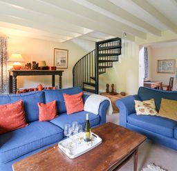 A living room with blue sofas and a wooden coffee table with wine and glasses near a black spiral staircase at Taibach in Dinas Cross