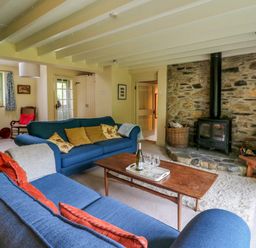 A living room with blue sofas a wooden coffee table stone fireplace and wood stove at Taibach in Dinas Cross
