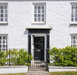 A white stone house front with black door and metal gate with green shrubs at Quay House in Charlestown