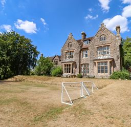 A large stone house with multiple windows and a pitched roof next to a grassy area with small soccer goals at Nethercott House Iddesleigh near Hatherleigh