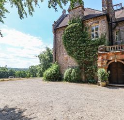 An old stone building with a gravel driveway green plants and trees in the background at Nethercott House in Iddesleigh near Hatherleigh
