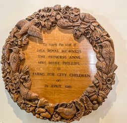 A carved wooden plaque with birds and flowers commemorating a visit by Princess Anne to Farms for City Children at Nethercott House Iddesleigh near Hatherleigh