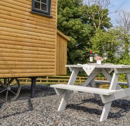 A wooden picnic table with a bottle of wine glasses and flowers next to a wooden wagon in a garden at Rose in Illogan