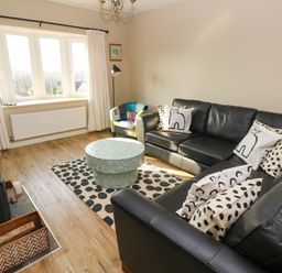 A living room with a black leather sofa and polka dot cushions a round patterned coffee table and a multicolor armchair at Sandtop in Tenby