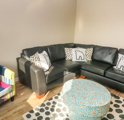 A corner with a black leather sectional sofa with patterned cushions a colorful patchwork armchair and a round patterned ottoman on a polka dot rug at Sandtop in Tenby
