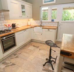 A kitchen with white cabinets wooden countertops and tiled floor at Sandtop in Tenby