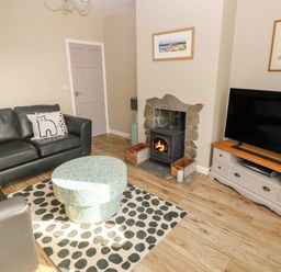 A living room with black sofas a round patterned ottoman a fireplace and a television on a cabinet at Sandtop in Tenby