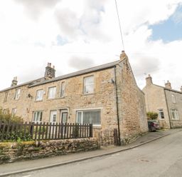 A street view of stone terraced houses with chimneys and a small front garden with a wooden fence at 4 Tyne View in Wark