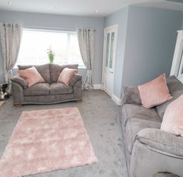 A living room with two grey sofas and pink cushions a pink rug on the floor and a window with curtains at 4 Tyne View in Wark