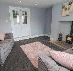 A living room with two sofas a pink rug a wood burning stove and double doors at 4 Tyne View in Wark