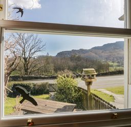 A window looking out to a garden with a bird feeder a wooden table a fence and hills beyond at Fellside View in Chapel Stile