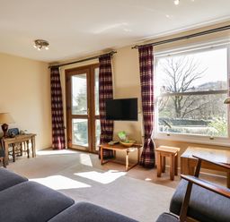 A living room with couch armchairs a small table a wall mounted TV and large windows with curtains at Fellside View in Chapel Stile