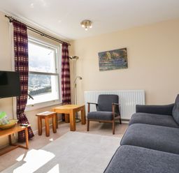 A living room with a gray sofa armchair wooden tables a TV and window with striped curtains at Fellside View in Chapel Stile