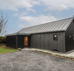 A black exterior building with a metal roof next to a gravel driveway and a small tree at Skylark in Bishop Wilton