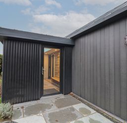 An exterior entrance with a glass door on a black corrugated wall and a small grassy area at Skylark in Bishop Wilton