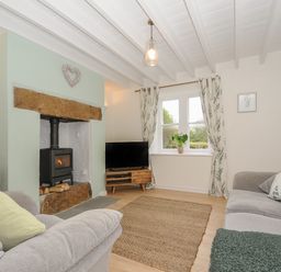 A living room with a wood stove fireplace two sofas a television and a window with curtains at Carvannel Cottages in North Cliffs near Portreath