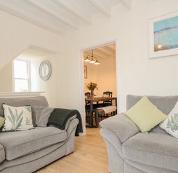 A living room with two gray sofas with green and white pillows and a view into a dining area at Carvannel Cottages North Cliffs near Portreath