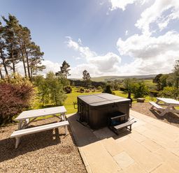 An outdoor area with a covered hot tub two white picnic tables gravel and stone flooring with trees and hills in the background at Heatherbrae in Middleton-In-Teesdale