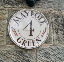 A ceramic house number plaque with the number 4 and text Maypole Green mounted on a stone wall at 4 Maypole Green in Fylingthorpe