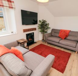 A living room with two gray sofas a red rug a wall-mounted TV and a plant at 4 Maypole Green in Fylingthorpe