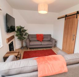 A small living room with two gray sofas a red rug a wooden sliding door and a wall-mounted television at 4 Maypole Green in Fylingthorpe