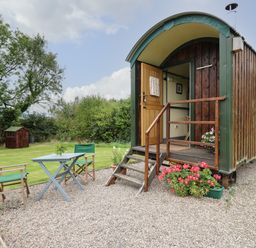 A shepherds hut with steps and flowers outside and a table with two chairs on gravel at Brown Hare Shepherds Hut in Llangorse