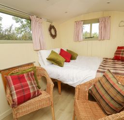 A small room with a bed and two wicker chairs with cushions at Tilly Gypsy-style Caravan Hut in Llangorse