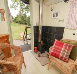 A small sitting area with wicker chairs and a wood stove with a chimney pipe at Tilly Gypsy-style Caravan Hut in Llangorse