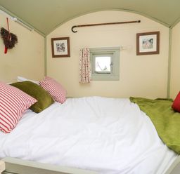 A bed with striped and solid pillows near a small window with curtains in a room at Sweet Briar Shepherds Hut in Llangorse
