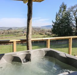 A hot tub on a wooden deck overlooking green fields and hills at Bryn Hafod in Llandrindod Wells