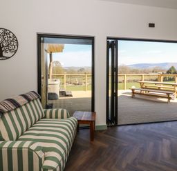 A room with a striped sofa and wooden side table opening to a deck with picnic benches at Llety Cariad in Llandrindod Wells