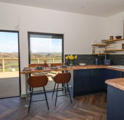A kitchen with wooden countertops, blue cabinets, bar stools, and a view of the countryside at Llety Cariad in Llandrindod Wells
