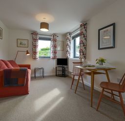 A living room with a red sofa two chairs a small wooden table and a television at Lillemor South Tawton near Whiddon Down