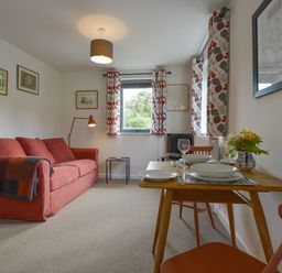 A sitting area with a red sofa and dining table set with plates and glasses at Lillemor in South Tawton near Whiddon Down