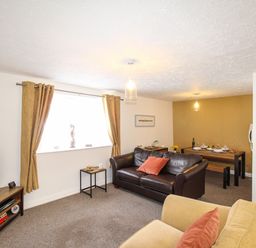 A living room with a brown leather sofa, beige armchairs, a wooden TV stand, and a dining table with tableware at Brewers Retreat in Weymouth