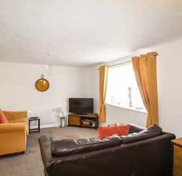 A living room with a brown leather sofa and orange upholstered armchair near a window with orange curtains at Brewers Retreat in Weymouth