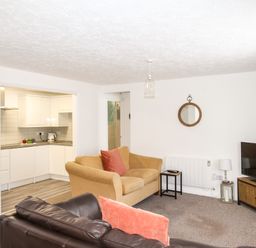 A living room with sofas and a TV cabinet next to an open kitchen at Brewers Retreat in Weymouth