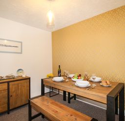 A dining room with a wooden table, bench seating, sideboard, patterned yellow wallpaper and table set with dishes and fruit at Brewers Retreat in Weymouth
