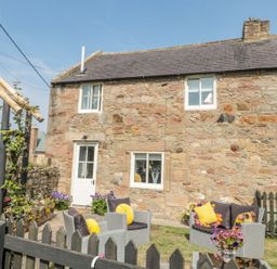 A stone cottage exterior with outdoor seating area and flowers at O'Neil Cottage in Beadnell