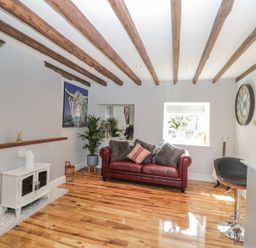 A living room with a red leather sofa wooden beams on ceiling a white stove and a large clock on the wall at O'Neil Cottage in Beadnell
