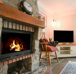 A living room with a stone fireplace fire burning a wooden rocking chair with cushions a television on a stand and a rug on the floor at Barley Cottage Weycroft near Axminster