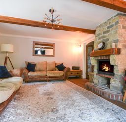 A living room with a stone fireplace two sofas a wooden chair and a rug at Barley Cottage in Weycroft near Axminster
