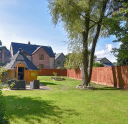 A garden with a tree a small cabin and outdoor seating in front of houses at Barley Cottage in Weycroft near Axminster