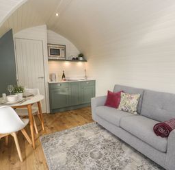 A small living space with a grey sofa, a round dining table with two chairs, and a kitchenette with green cabinets at Yr Onnen in Bontuchel near Ruthin
