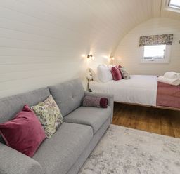 A bedroom with a gray sofa a bed with white linens and pillows a window and wooden floor at Yr Onnen in Bontuchel near Ruthin