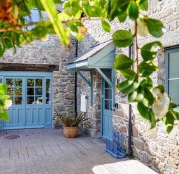 An outdoor stone patio with blue doors and windows framed by leafy branches at Trelawney Mawnan Smith Near Falmouth