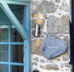 A close up of a stone wall with a metal light fixture and a sign reading Trelawney next to a blue wooden door frame at Trelawney Mawnan Smith Near Falmouth