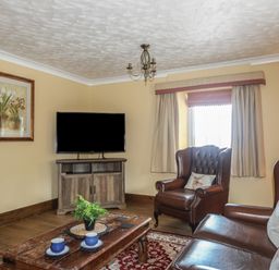 A living room with leather armchairs a wooden coffee table with cups a television and a window at Frongoch Cottage in Red Wharf Bay near Pentraeth