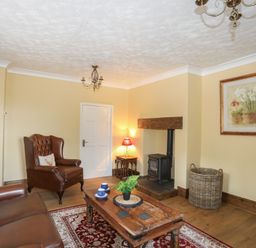 A living room with leather chairs wooden coffee table stove and floral painting at Frongoch Cottage in Red Wharf Bay near Pentraeth